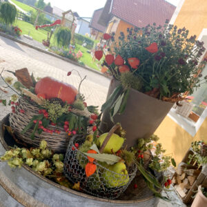 Ein Hauch von Herbst! Auf rustikalen Holzfässern sind verschiedene herbstliche Deko-Elemente arrangiert. Bunte Kürbisse in allen Formen und Größen, getrocknete Maiskolben, duftende Zimtstangen und dekorative Blätter sorgen für eine gemütliche Atmosphäre.